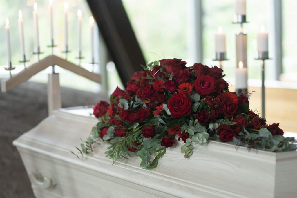 Stor baaredekorasjon med roede roser til begravelse paa hvit kiste