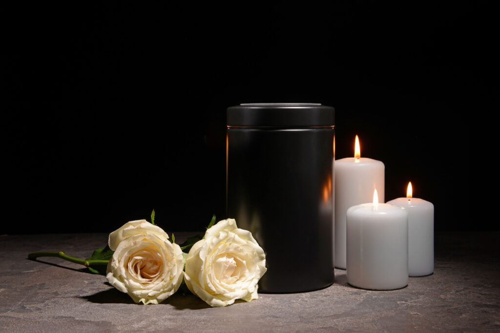 en moerk urne oppstilt med hvite roser og hvite kubbelys paa hver side. 